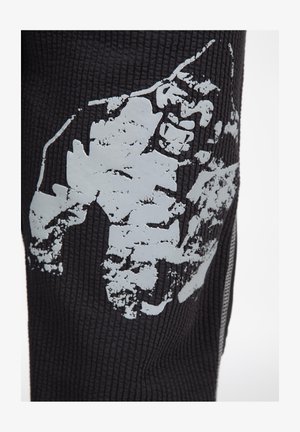 Zwarte gemarmerde stof met een groot, verweerd grijs graphic. Het ontwerp benadrukt een robuuste, abstracte vorm op het oppervlak.