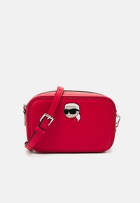 Czerwona skórzana torebka na krzyż z zamkiem błyskawicznym, z przypinką z postacią z kreskówki. Regulowany pasek i gładka tekstura.