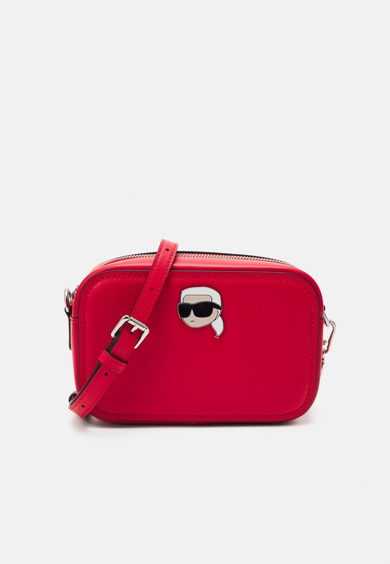 Czerwona skórzana torebka na krzyż z zamkiem błyskawicznym, z przypinką z postacią z kreskówki. Regulowany pasek i gładka tekstura.