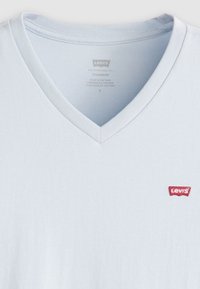 Lyseblå bomull V-hals t-skjorte med ribbestrikket krage, med en liten rød Levi's-logo på venstre side. Glatt tekstur, standard passform.
