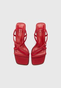 Rote vegane Sandalen mit quadratischer Zehenpartie, ausgestattet mit mehreren schmalen, überkreuzten Riemen und einer glatten, matten Oberfläche. Flache Sohle mit minimalem Profil.