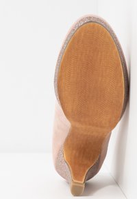 Talons en daim rose avec une semelle en bois lisse, ornés d'un bord brillant et étincelant. Bout arrondi et design minimaliste.