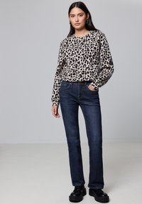 Sudadera de leopardo en color beige y negro, combinada con jeans rectos de color azul oscuro. La modelo lleva puestos zapatos de plataforma negros.