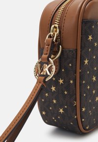 Borsa in pelle marrone e tessuto scuro a motivo, caratterizzata da accenti dorati a forma di stella, zip dorata e dettaglio hardware circolare con logo MK.
