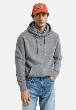 Grijze katoenen hoodie met koordjes en een voorzak, voorzien van een reliëf "GANT" logo. Gecombineerd met lichtblauwe spijkerbroek.
