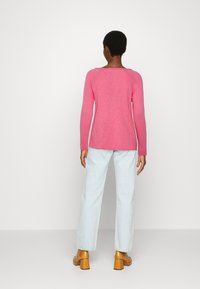 Pink long-sleeve shirt in a soft texture, paired with light blue straight-leg jeans and brown chunky-heeled shoes.