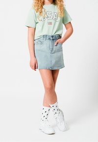 Camiseta verde menta con la impresión "USA" y la bandera, combinada con una falda de mezclilla azul clara. Zapatillas blancas y calcetines blancos con rayos negros.