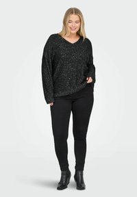 Melnas, mirdzošas, ar V veida kaklu, brīva griezuma adīta džemperis ar garām piedurknēm, saskaņots ar pieguļošām melnām džinsām un potīšu zābakiem.