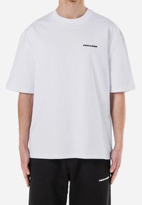 Vit bomull t-shirt med avslappnad passform, med en svart "PEGADOR" logotyp på vänster bröst. Designen har korta ärmar och rundad halsringning.