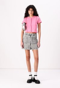 Ροζ κοντό μπλουζάκι με λεπτομέρεια ραφής μπροστά, συνδυασμένο με γκρι τζιν φούστα με μπροστινά κουμπιά και τσέπες, φορεμένο με μαύρες πλατφόρμες.