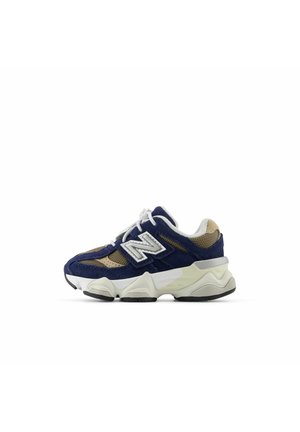 Baskets New Balance bleu marine et beige avec lacets blancs, tige en mesh et suède, et semelle blanche épaisse avec crampons noirs.
