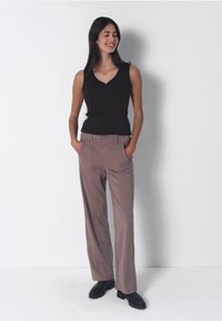 Musta hihaton toppi yhdistettynä vaaleanruskeisiin korkea vyötäröisiin housuihin, joissa on taskut ja sileä rakenne, täydentäen mustilla kengillä.