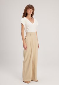 Witte V-hals t-shirt met textuur bloemaccenten op de schouders en hooggeplaatste beige wijde broek. Gladde stof en een ontspannen pasvorm.