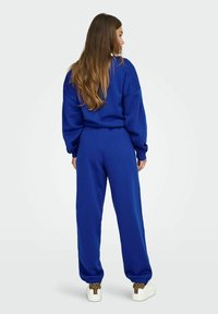 Niebieska bluza i dopasowane spodnie wykonane z miękkiego materiału. Spodnie dresowe mają elastyczne mankiety, a sneakersy mają akcent w panterkę na pięcie.