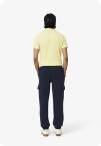 Geel polo shirt met korte mouwen en marineblauwe cargobroek met zijzakken; de broek heeft elastische boorden en een relaxte pasvorm. Witte sneakers zichtbaar.