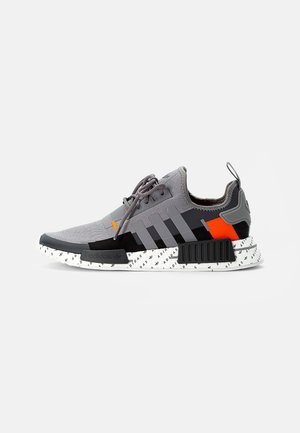 Szare i czarne buty sportowe Adidas z pomarańczowym akcentem, sznurowane, z trzema paskami po boku i białą podeszwą środkową zdobioną tekstem "Adidas".
