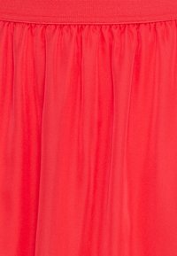 Gros plan sur un tissu plissé rouge avec une taille froncée, montrant des plis verticaux lisses et une texture douce.