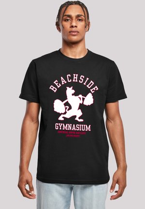 Sort bomulds T-shirt med et hvidt og lyserødt grafisk design af en løve, der løfter vægte, med teksten "BEACHSIDE GYMNASIUM" ovenfor.