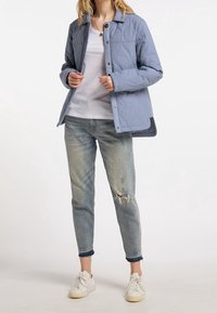 Jasnoniebieska pikowana kurtka z zatrzaskami, noszona na białym t-shircie i zniszczonych jasnoniebieskich dżinsach, zestawiona z białymi trampkami.