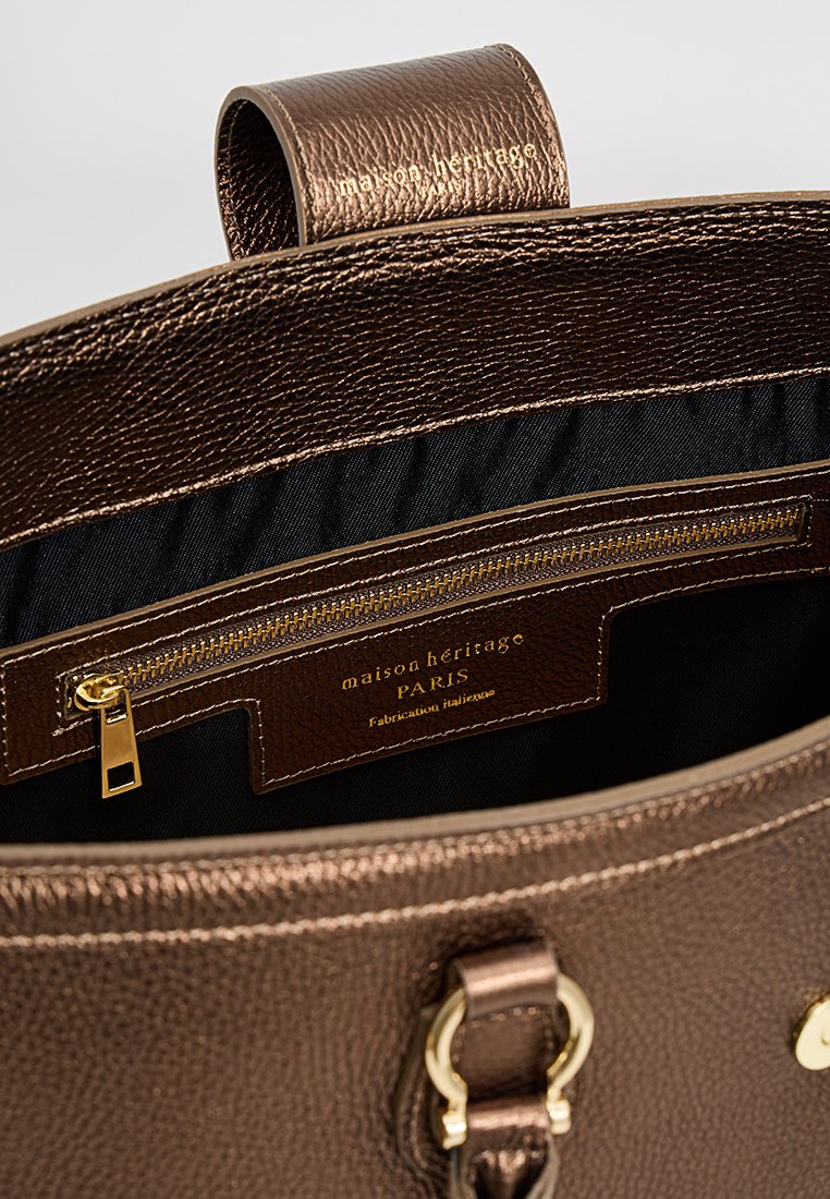 Sac à main en cuir marron texturé avec un compartiment zippé, des accents en métal doré et une doublure intérieure noire. Logo et étiquette visibles à l'intérieur.