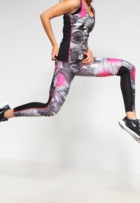 Zwarte en gemusterde sportoutfit bestaande uit een grijs en roze bloemenontwerp. De tanktop heeft dunne bandjes en de leggings zijn aansluitend.