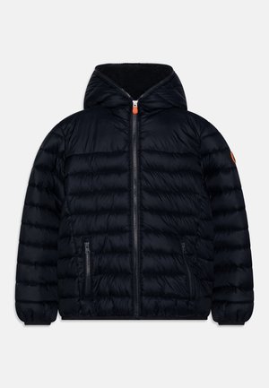 Doudoune matelassée noire à capuche avec fermeture éclair frontale, poches latérales zippées, poignets élastiques, tirette de fermeture éclair orange et patch sur la manche.