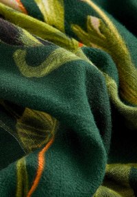 Gros plan d’un tissu vert à texture douce montrant un motif floral dans des tons jaunes et oranges.