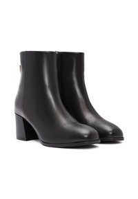 Botas de tobillo de cuero negro con un respaldo texturizado, punta redondeada y un tacón grueso. Presentan una cremallera lateral y un detalle de hardware minimalista.