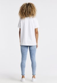 Camiseta de algodón blanca de manga corta, combinada con jeans skinny azul claro y zapatillas blancas, vista desde atrás.
