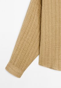 Beige strukturerad långärmad skjorta med en ribbad mönster, som har en manschettärm och en rak fåll. Tillverkad av ett lätt vävt material.