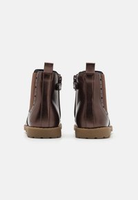 Botas de cuero marrón hasta el tobillo con lados elásticos en tono marrón claro, cierre de cremallera y suelas de goma. Detalle de costura notable a lo largo de los lados.