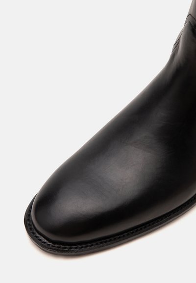 Gros plan de l'avant lisse et arrondi d'une chaussure en cuir noir poli avec des coutures visibles le long du bord de la semelle.