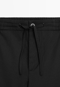 Shorts neri con tessuto testurizzato, cintura elastica, lacci e chiusura con bottone. Senza tasche o motivi visibili.