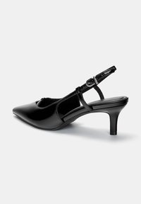 Chaussure slingback en cuir verni noir avec un bout pointu, un petit talon aiguille et une sangle réglable à boucles. Texture lisse avec un minimum de détails.