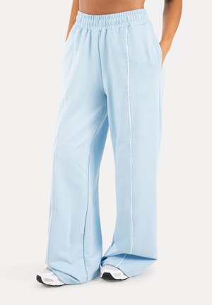 Hellblaue weit geschnittene Jogginghosen mit weißen Nahtdetails, elastischem Bund, Seitentaschen, getragen mit weißen Sneakern.