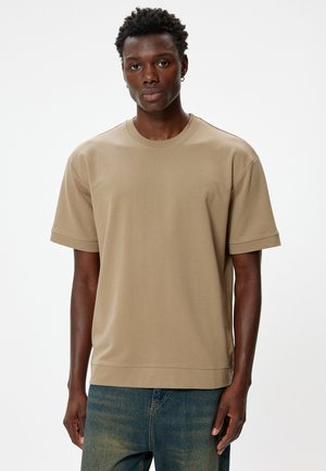 Beige t-shirt med korte ærmer, lavet af blødt stof, med en rund halsudskæring og en afslappet pasform. Båret med blå slidte jeans.
