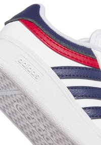 Sneaker bianca con accenti blu navy e rossi, suola testurizzata, tre strisce blu navy e logo "adidas" in rilievo sul lato. Finitura in pelle liscia.