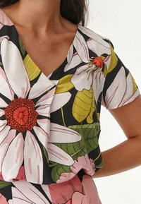 Blomstret bluse med v-udskæring, sort baggrund, store lyserøde og hvide blomster samt grønne blade. Letvægtigt stof, korte ærmer.