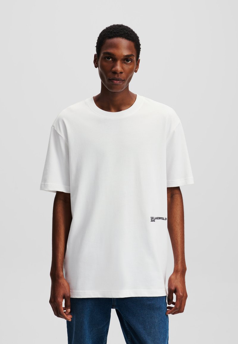 Biela bavlnená tričko s krátkymi rukávmi, vo voľnom strihu, okrúhlym výstrihom a malým čiernym logom na spodnej ľavej strane.