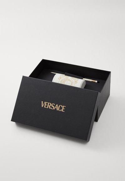Versace branded black box containing a white cylindrical item with gold accents and a patterned design, accompanied by a pen.