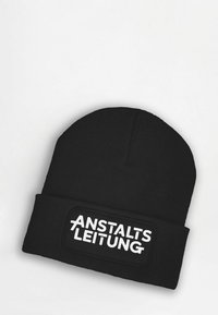 Black knitted beanie with a folded cuff featuring a rectangular patch with the text "ANSTALTSLEITUNG" in bold white letters.