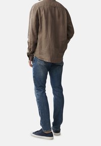 Hnědá lněná košile s kulatým lemem, ve spojení s modrými džínami a námořnickými teniskami. Košile má dlouhé rukávy a manžety na knoflíky.