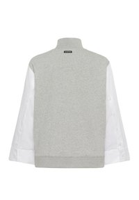 Sweat-shirt gris avec un col montant, des manches blanches contrastantes avec boutons, et un corps en molleton texturé. Comprend un ourlet côtelé et une étiquette de marque sur le col.
