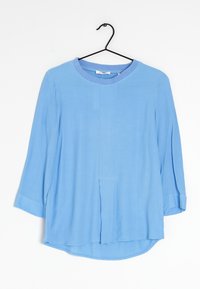 Himmelblaue Bluse mit langen Ärmeln und rundem Halsausschnitt, ausgestattet mit einer vorderen Naht und Faltendetails. Hergestellt aus einem glatten, weichen Stoff.