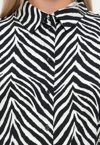 Μαύρη και λευκή μπλούζα με ρίγες ζέβρας, με μυτερό γιακά, μπουτόν μπροστά και απαλή, υφασμάτινη υφή.