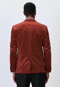 Roter Blazer mit Muster, glatter Textur, tailliertem Schnitt, zwei Rückenventilatoren und Knopfakzenten an den Ärmeln.