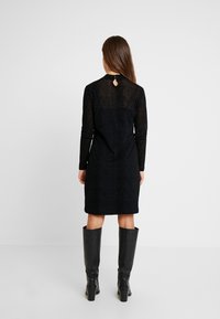 Svart långärmad klänning med en strukturerad mönstring, knälång, med en liten nyckelhålsdetalj på baksidan. Matchad med höga svarta stövlar.