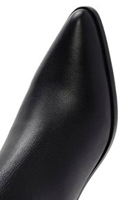 Zapato negro de cuero con punta afilada, textura suave, silueta esbelta y diseño minimalista. Cuenta con un tacón bajo y líneas limpias.