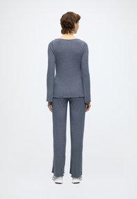 Σετ δύο τεμαχίων με ραβδώσεις από απαλό γκρι ύφασμα. Το τοπ διαθέτει στρογγυλή λαιμόκοψη και μακριά μανίκια. Το παντελόνι είναι ελαφρώς φαρδύ με ανοιχτές ραφές και πλαϊνές σχισμές.