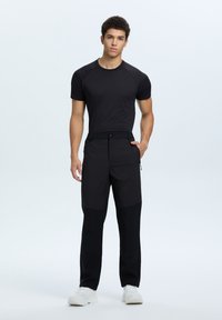 Zwart sport t-shirt met raglanmouwen en zwarte broeken met contrasterende stofpanelen en ritszakken, gecombineerd met witte sneakers.
